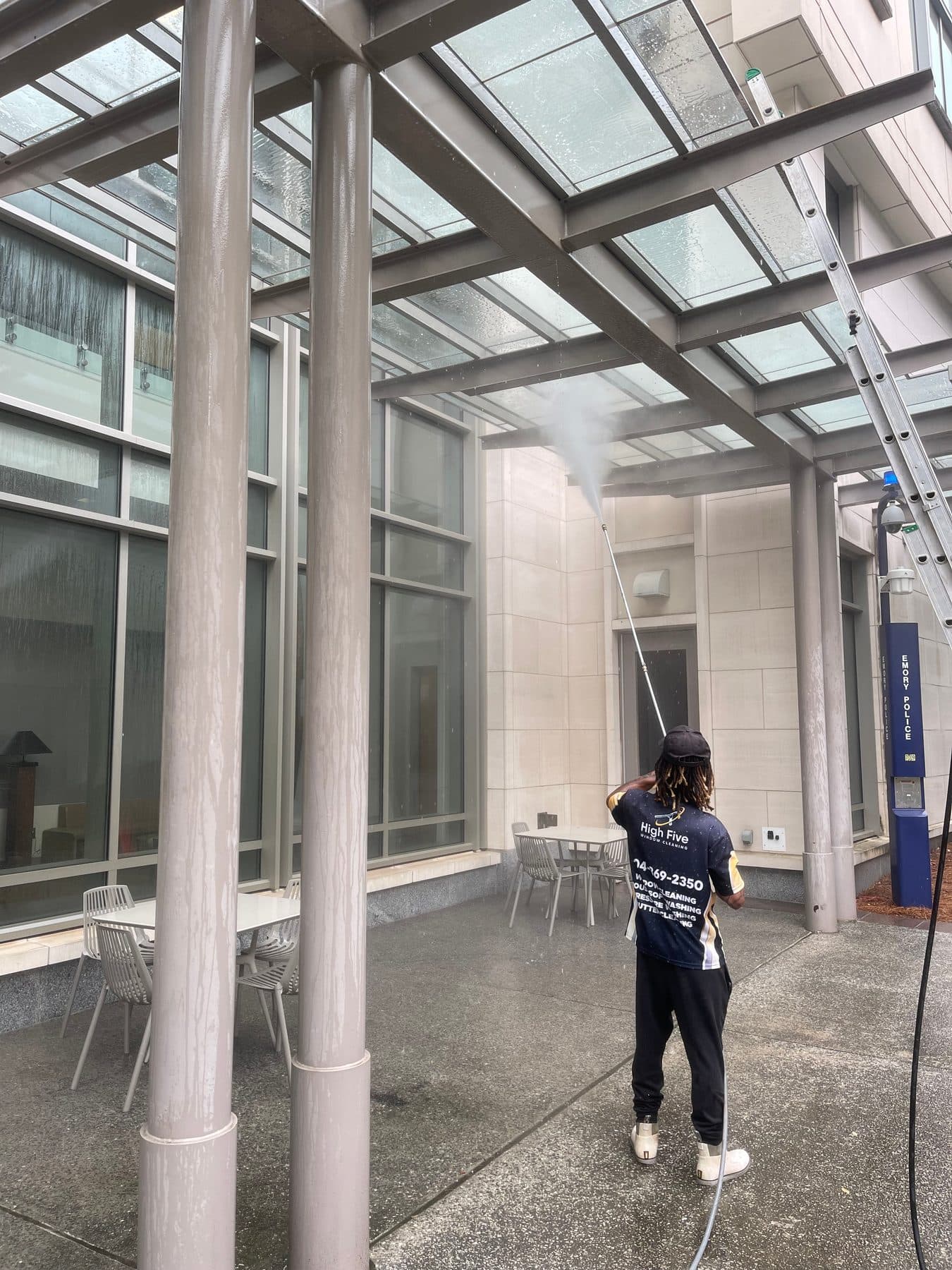 A High Five cleaner rinsing a glass canopy outside an office building