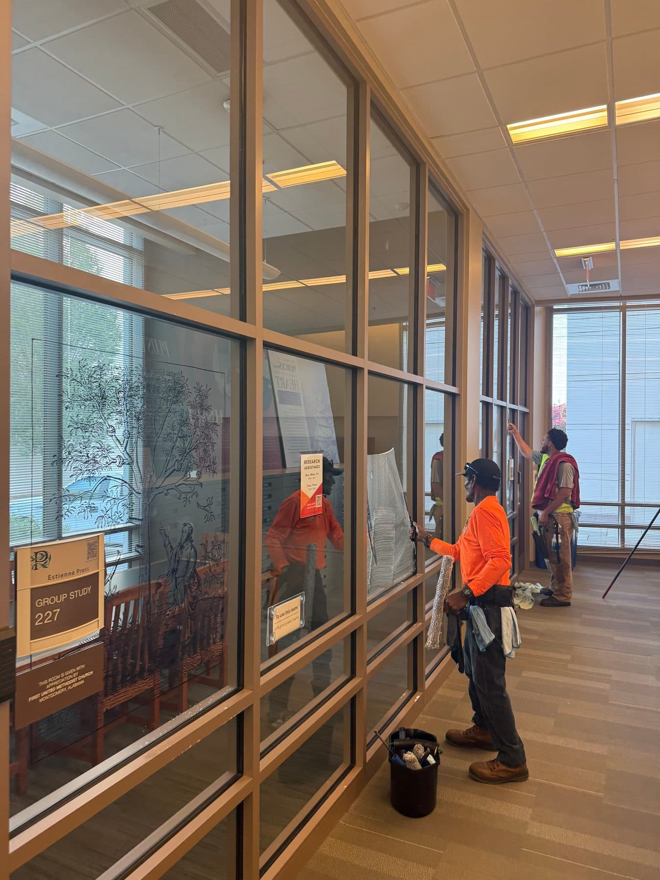Two cleaners washing an interior glass wall in an office hallway