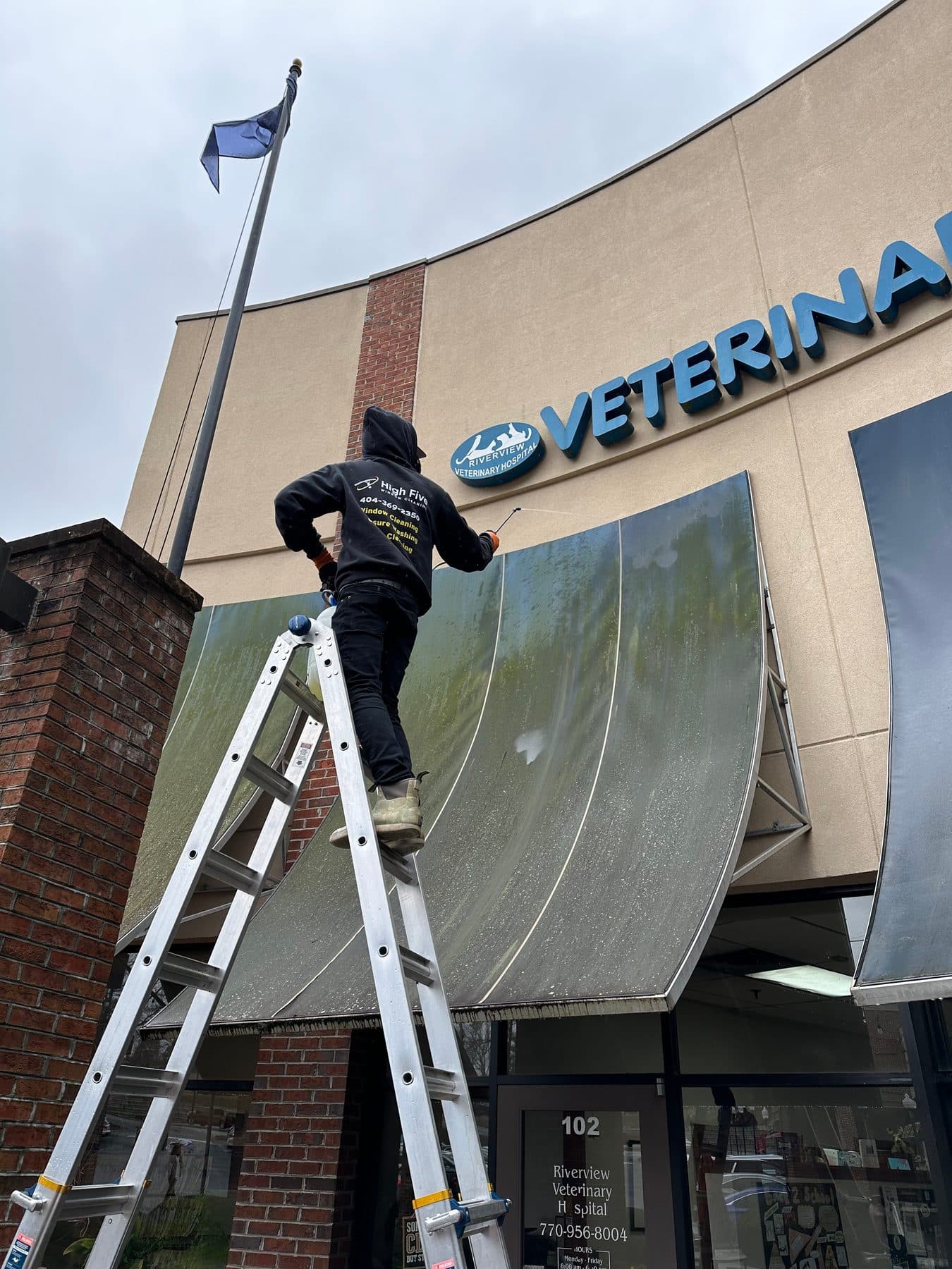 A High Five cleaner on a ladder doing storefront awning cleaning at a veterinary clinic