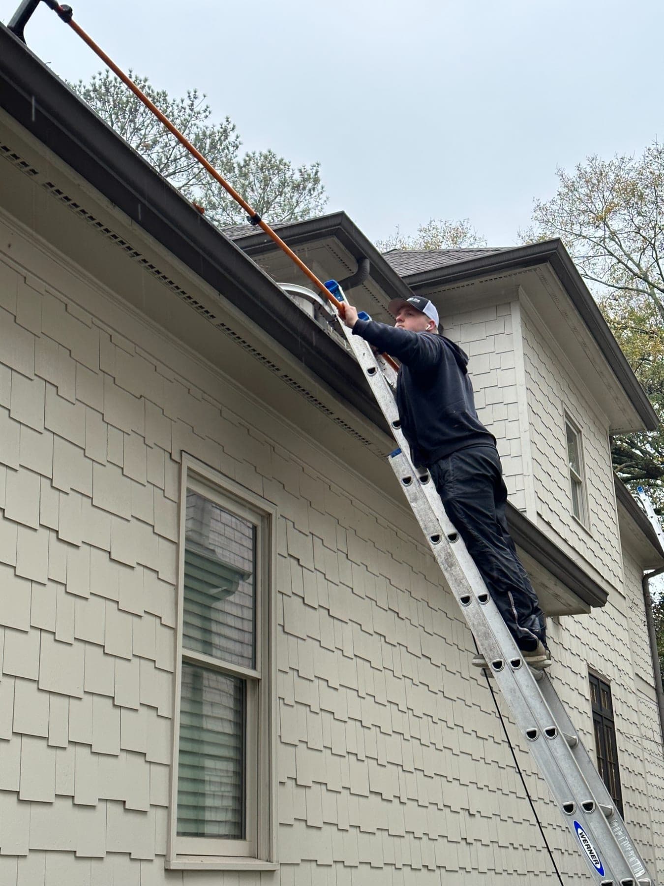 A High Five cleaner on a ladder, clearing a gutter with a pole