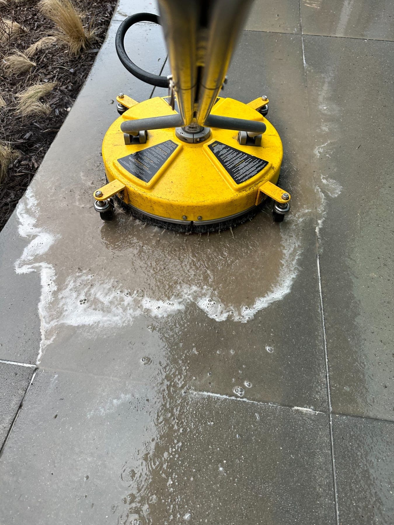A yellow surface cleaner lifting dirt off a concrete patio